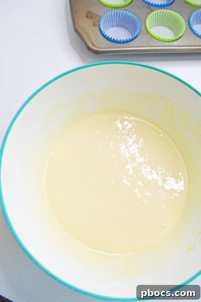 Chicka Boom Alphabet Treats 4 Cupcake batter being spooned into paper liners in a muffin tin, ready for baking.