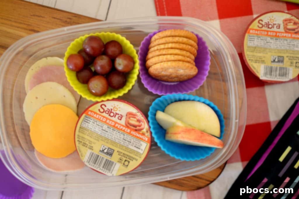 An assembled DIY lunchable featuring crackers, ham, cheese, grapes, and carrots with a dip.