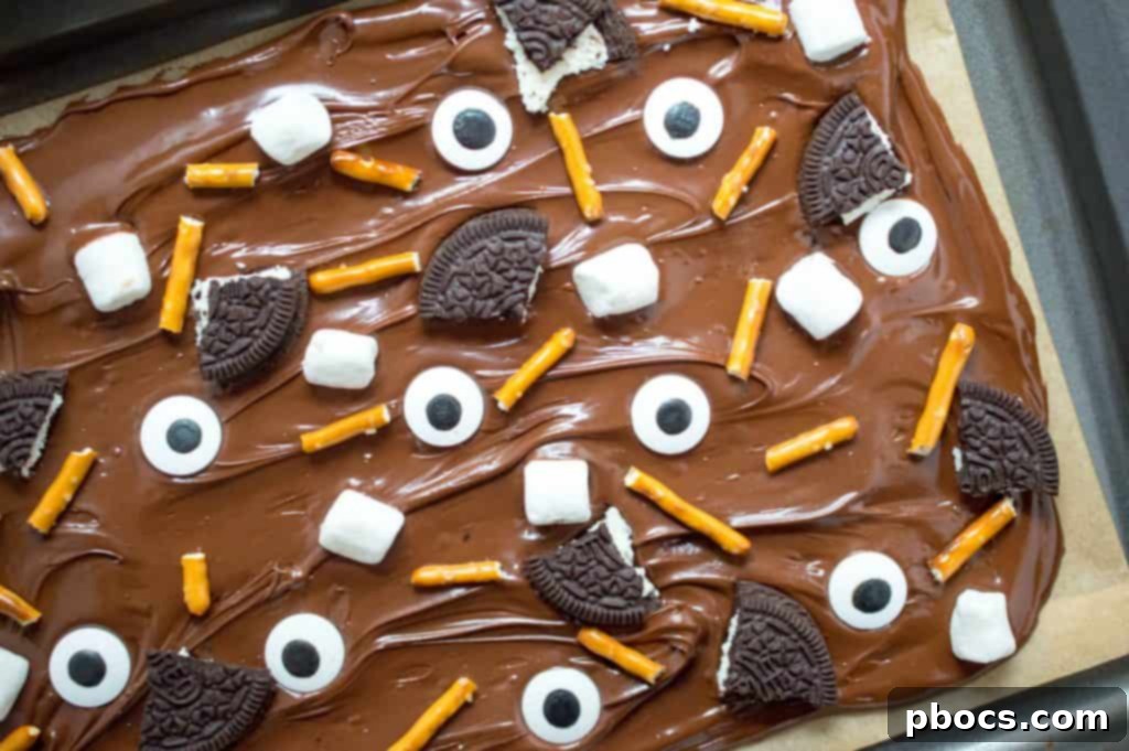 Decorating Halloween chocolate bark with assorted candy eyes and marshmallows