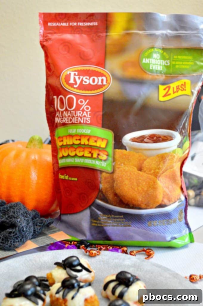 A child's hand reaching for a plate of Halloween spider chicken nuggets.