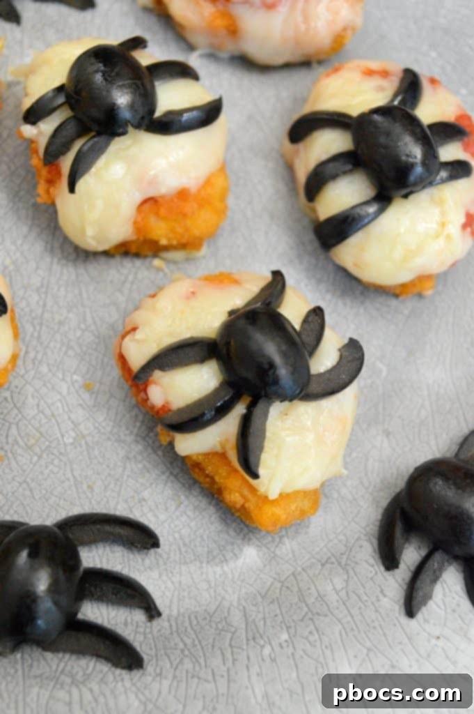 Black olive halves placed on cheesy chicken nuggets as spider bodies.