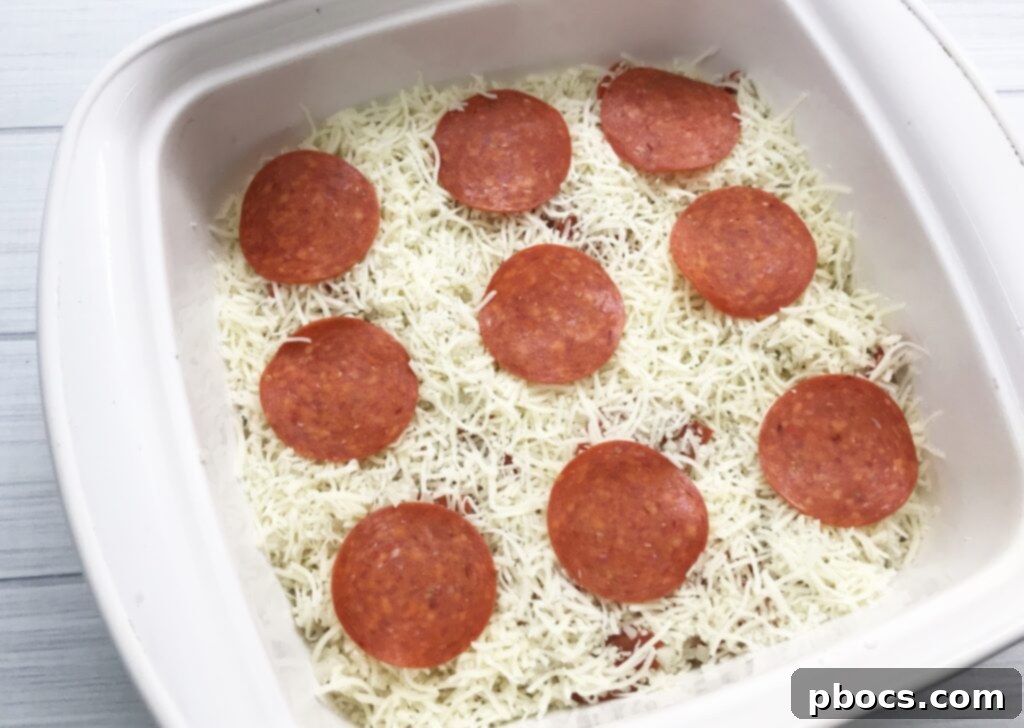 Spreading the Keto Pizza Casserole mixture evenly in a baking dish before adding the final cheesy toppings