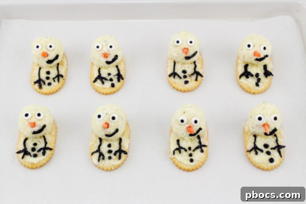 Frosty's Farewell Cheeseball 9 Piping black cream cheese details: arms, buttons, and a smile onto the snowman cheeseballs.