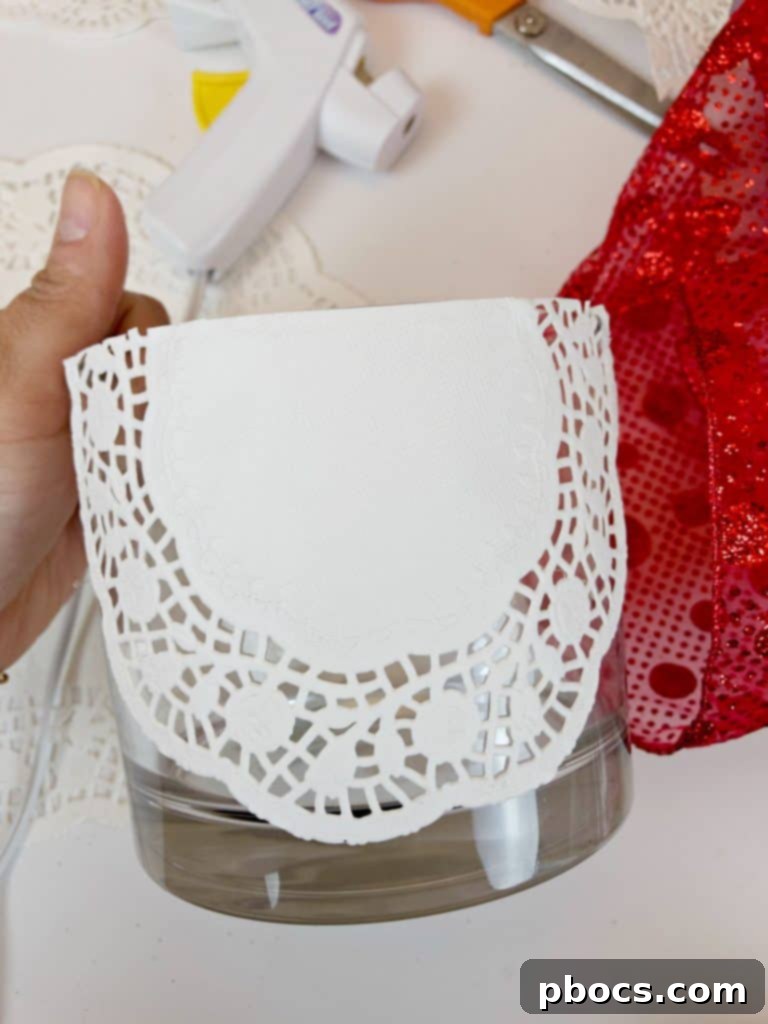 Homemade Valentine's Treat Dish 7 Gluing the carefully cut doily paper onto the rim of the glass vase, ensuring a smooth and even application.