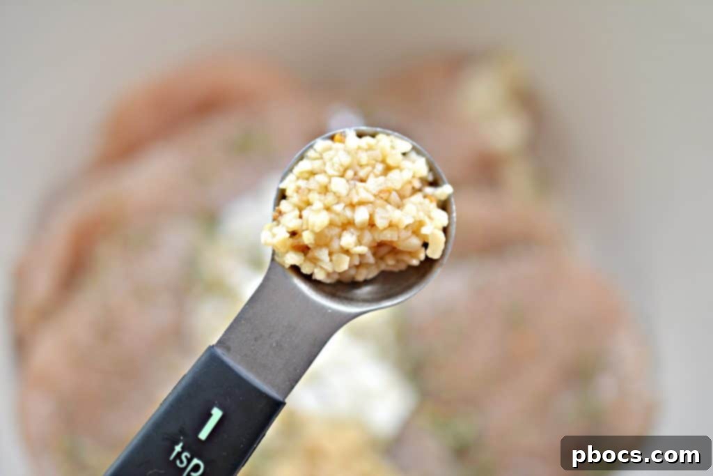 Adding minced garlic and the first tablespoon of olive oil to the chicken marinade.