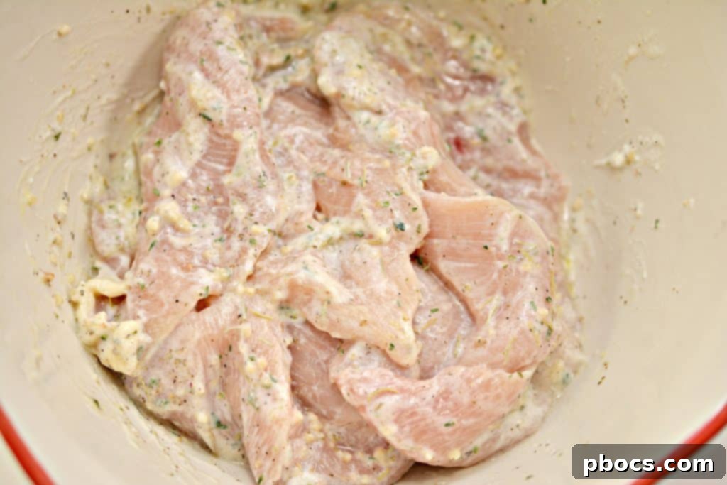 Ensuring each piece of chicken is fully and evenly coated with the Greek herb marinade.