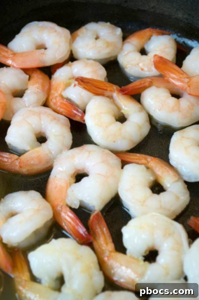 Shrimp cooking in a skillet with butter, preparing for the creamy lemon parmesan sauce.