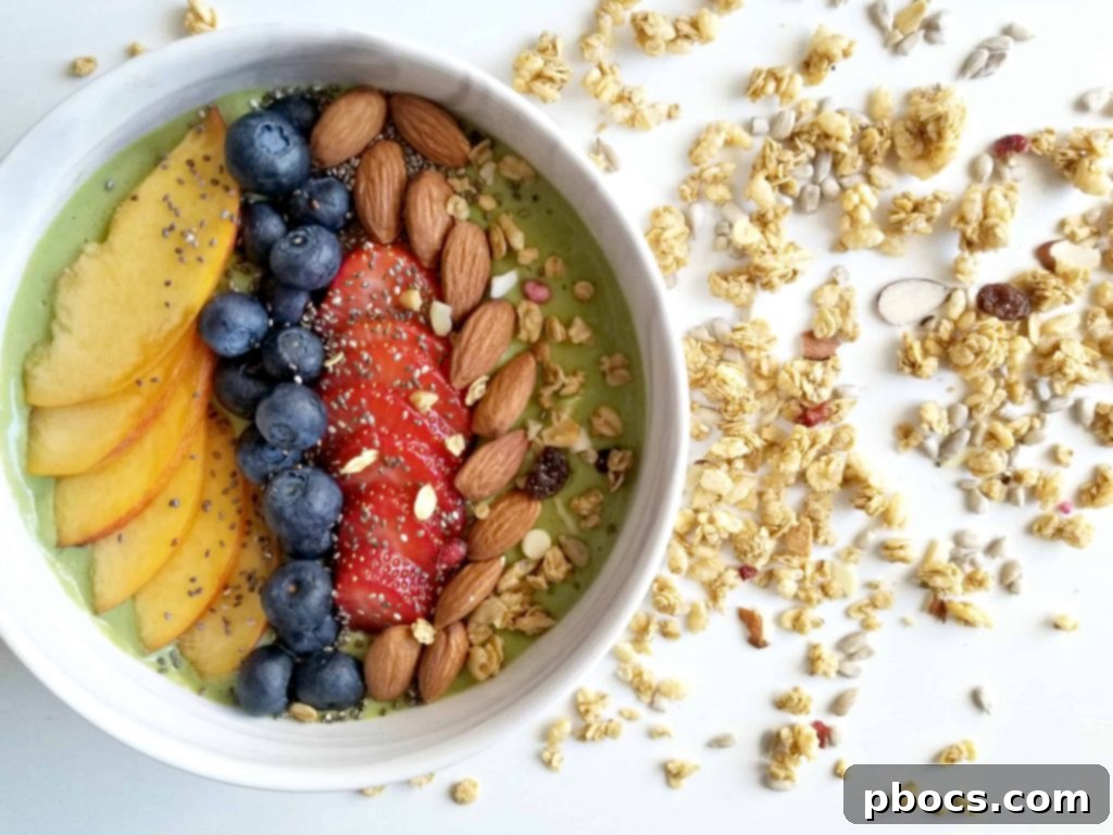 Hand holding a spoon in a delicious green smoothie bowl garnished with fruit, granola, and almonds