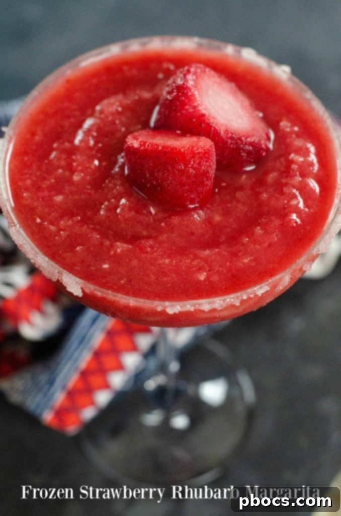 Vibrant Frozen Strawberry Rhubarb Margarita in a salt-rimmed glass, garnished with fresh fruit