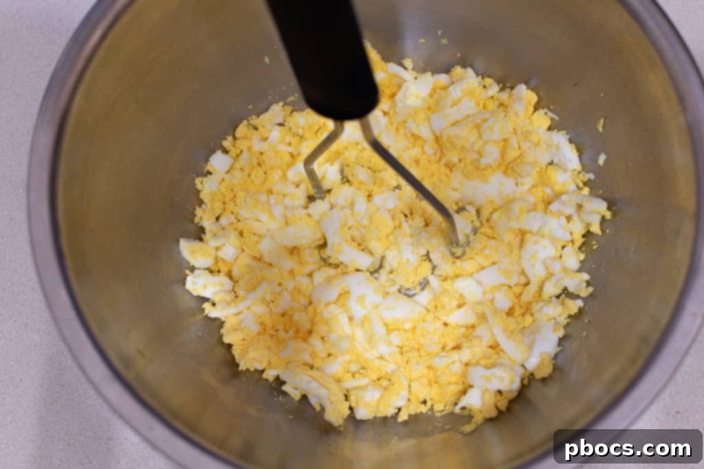 Adding mashed eggs to a mixing bowl