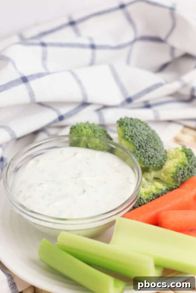 Overhead view of a white bowl filled with creamy Greek Yogurt Veggie Dip, garnished with a sprinkle of herbs