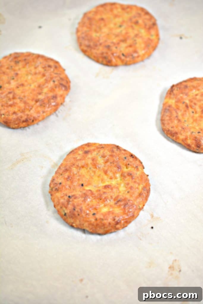 Four portions of keto cheese bun mixture pressed into rounded shapes on a parchment-lined baking sheet, ready for the oven.