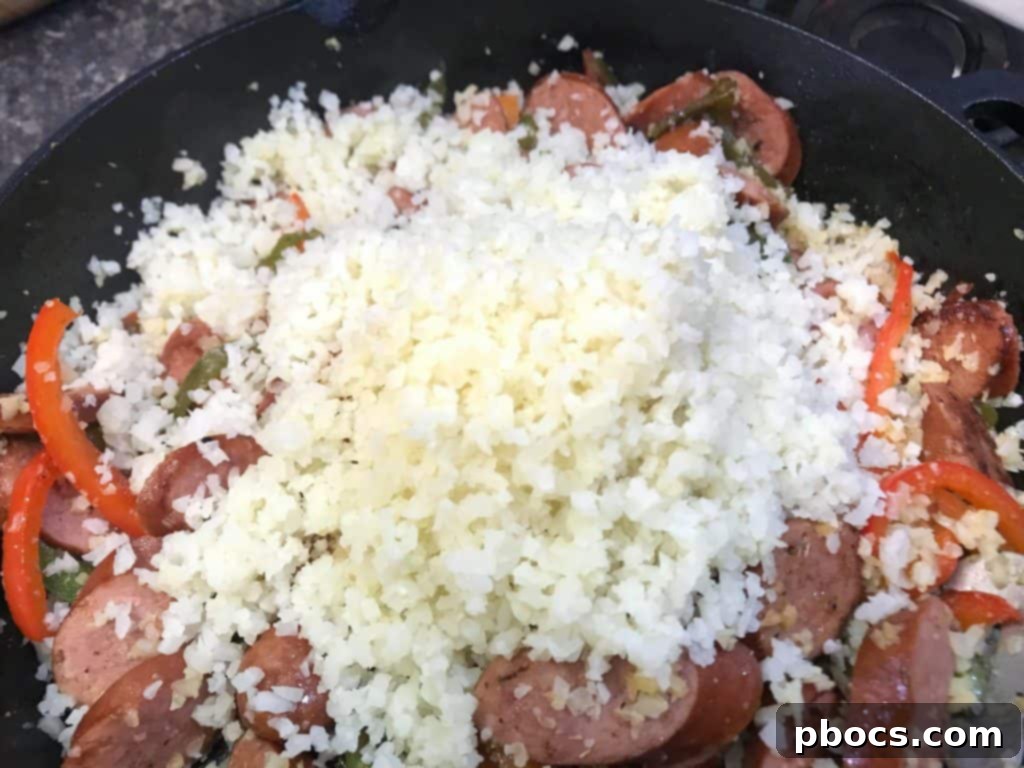 Mixing Cauliflower Rice, Kielbasa, and Bell Peppers in a Skillet for a Low Carb Dinner