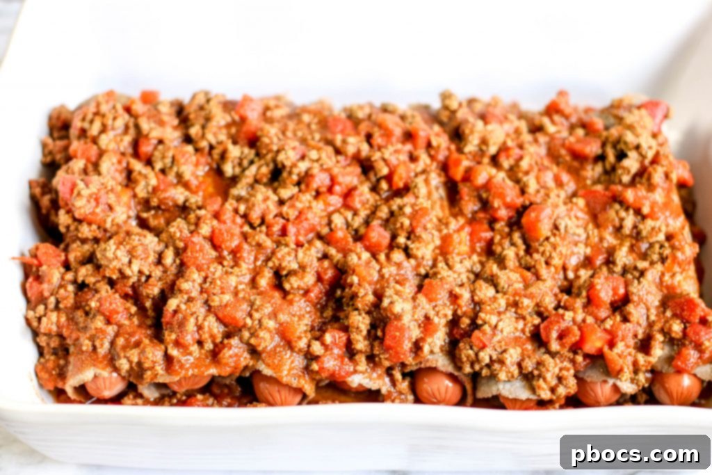 Hot dogs wrapped in tortillas placed in a casserole dish over chili.