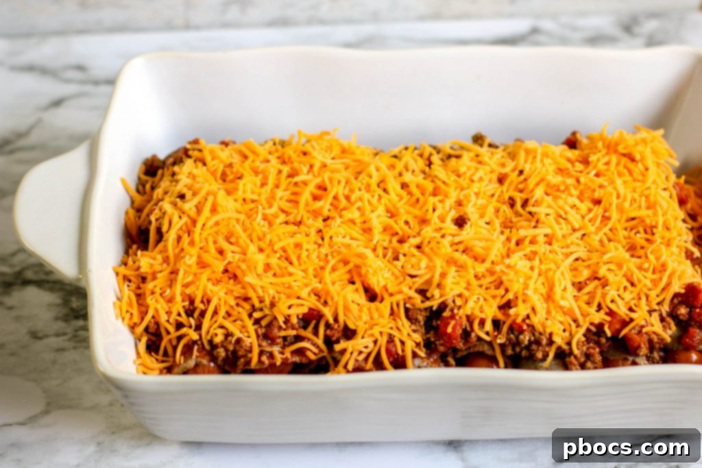 Pouring chili over hot dogs in a casserole dish.