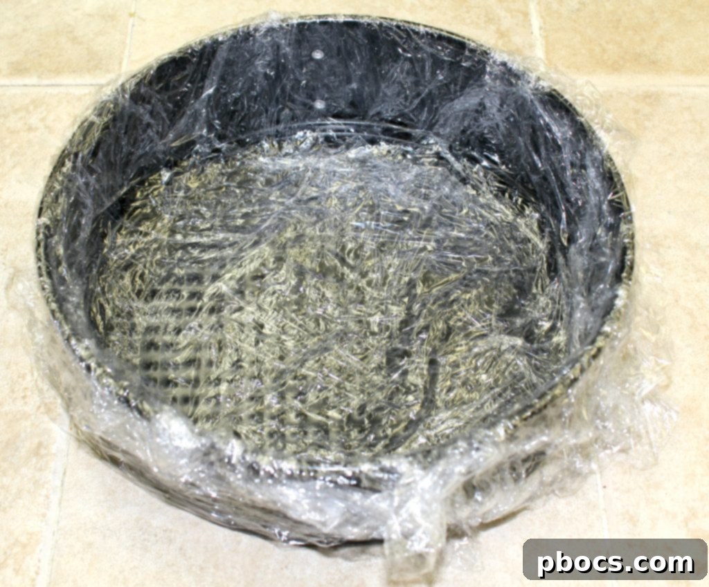 Lining a springform pan with plastic wrap for keto cheesecake.