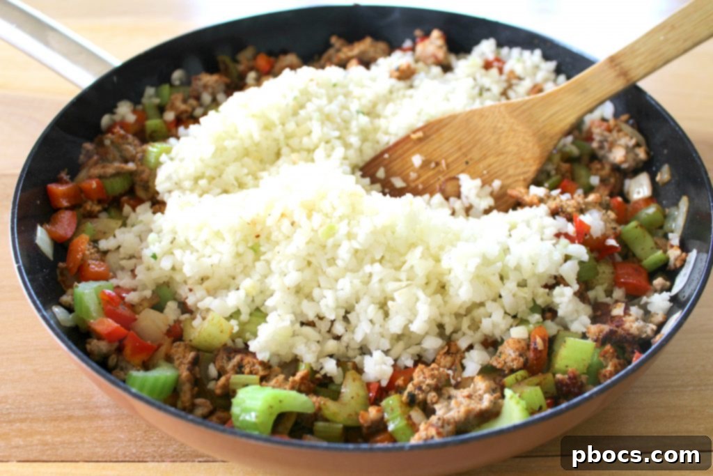Adding frozen cauliflower rice and chicken stock to the seasoned meat and vegetable mix