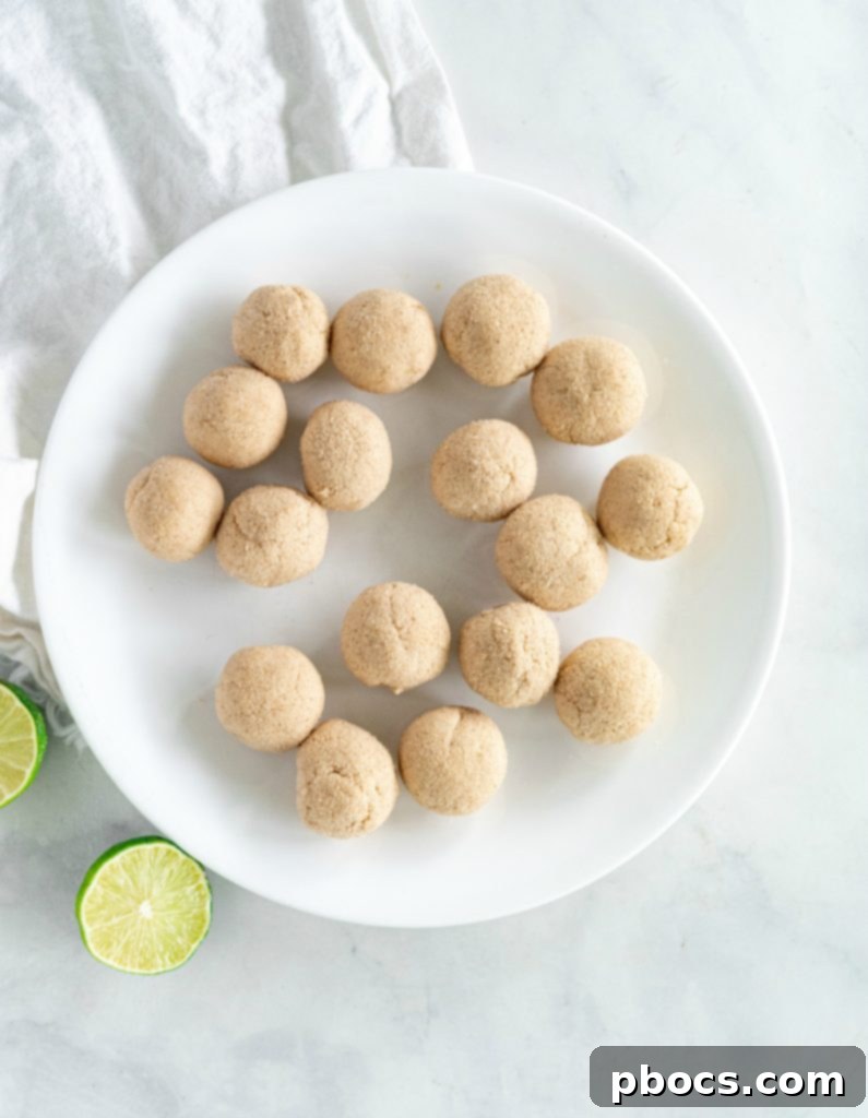 Refreshing Keto Key Lime Fat Bombs 13 Hands rolling a Keto Key Lime Fat Bomb in a shallow dish of shredded coconut for coating.