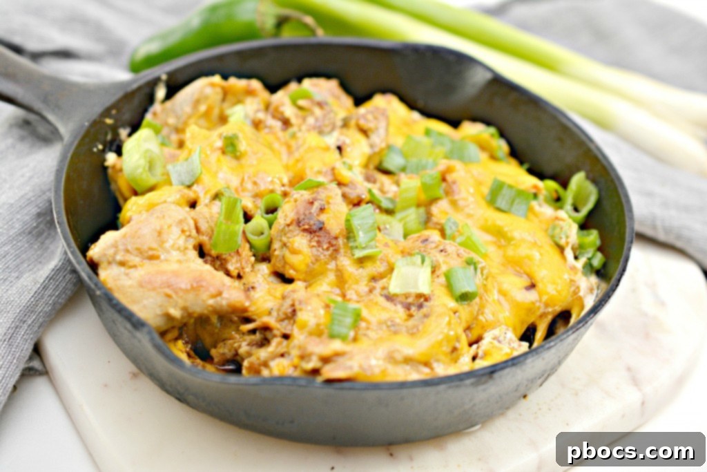 Keto Jalapeno Popper Chicken Skillet 6 A vibrant skillet of Low Carb Jalapeno Popper Chicken, generously topped with shredded cheddar cheese, ready for baking