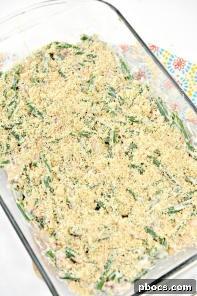 Spicy Keto Jalapeno Popper Green Bean Casserole 14 Step-by-step photo of pork rind crumbs and parmesan cheese being sprinkled over the green bean casserole before baking