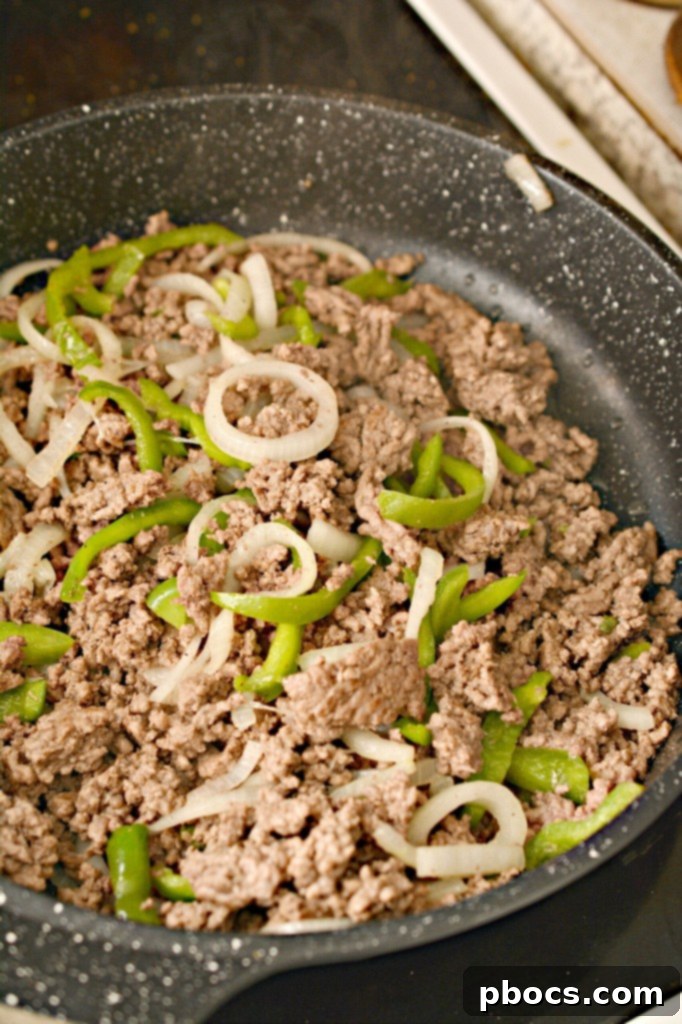 Ground beef, onions, and bell peppers cooking together in a large skillet
