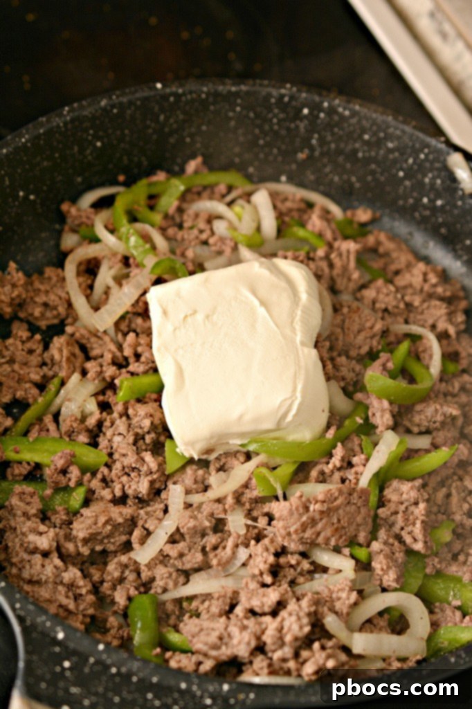 Stirring the cream cheese into the beef mixture until it is fully melted and smooth