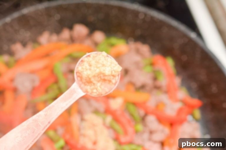 Adding minced garlic to the skillet with beef and vegetables