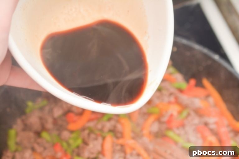 Pouring sauce into the skillet with Thai Basil Beef ingredients
