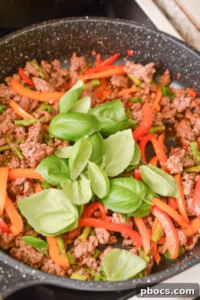 Fresh Thai Basil leaves being stirred into the skillet