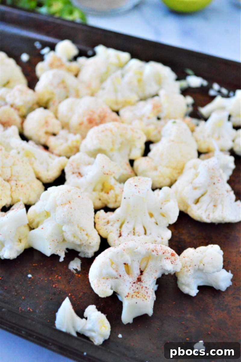 Cauliflower florets spread on a baking sheet, drizzled with olive oil and sprinkled with chili powder, ready for the oven.