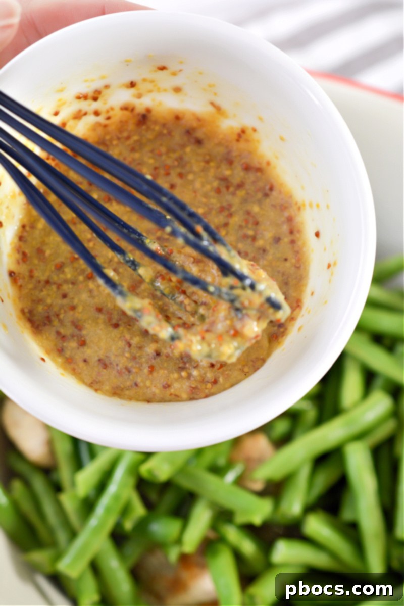 Tossing chicken and green beans with the keto honey mustard sauce in a mixing bowl.