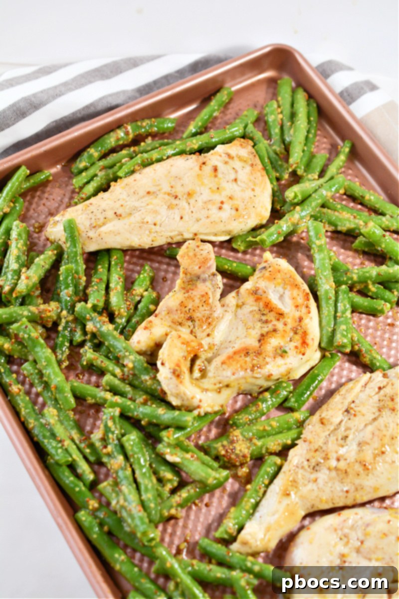 Chicken and green beans arranged in a single layer on a foil-lined sheet pan, ready for the oven.