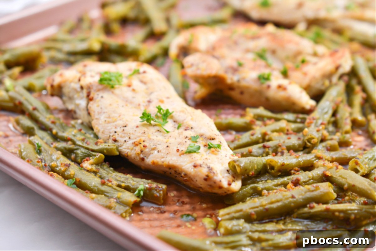 Sheet pan with chicken and green beans covered with foil, baking in the oven.