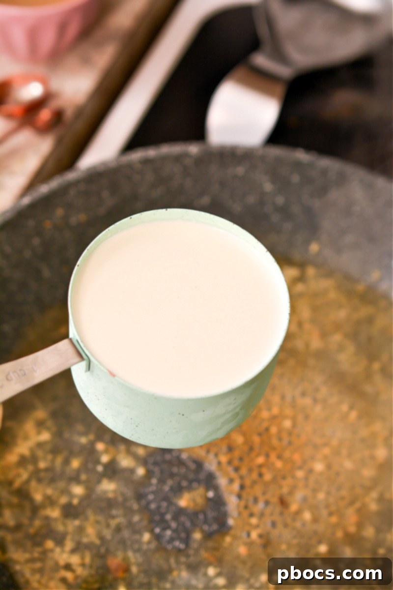 Comforting Keto Tuna Bake 19 Heavy whipping cream, Parmesan cheese, and chicken broth being whisked together in a skillet to form a creamy sauce.