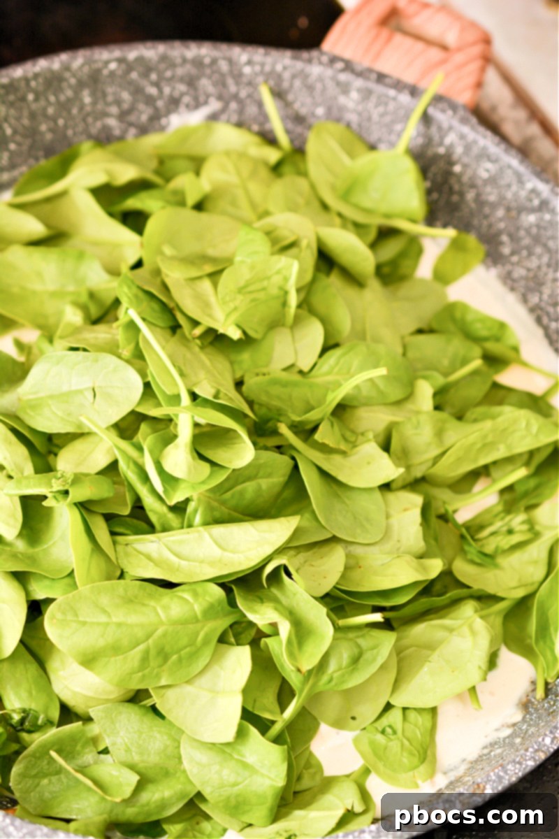 Comforting Keto Tuna Bake 21 Spinach and Palmini noodles added to the creamy sauce in the skillet, starting to wilt.