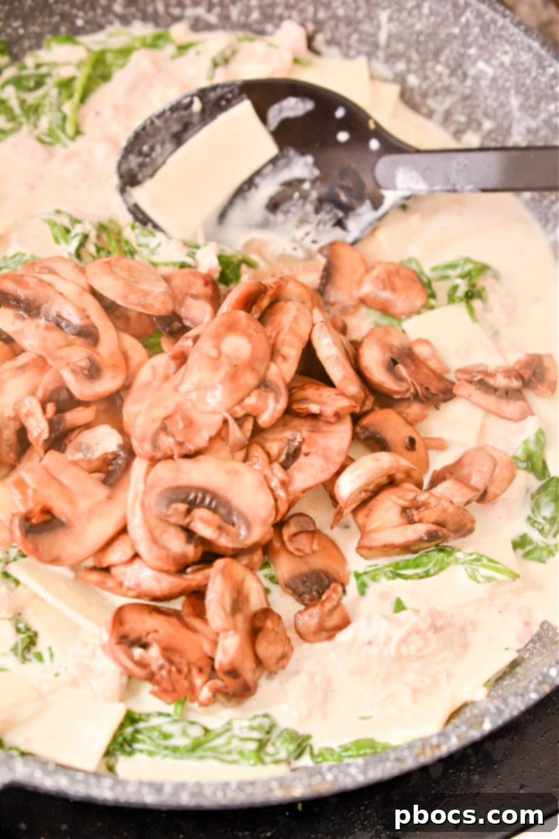 Comforting Keto Tuna Bake 22 Tuna, mushrooms, and crumbled bacon being stirred into the skillet with the creamy noodle and spinach mixture.