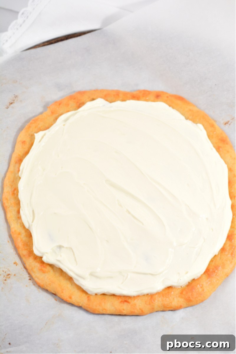 Applying cream cheese icing to keto fruit pizza crust