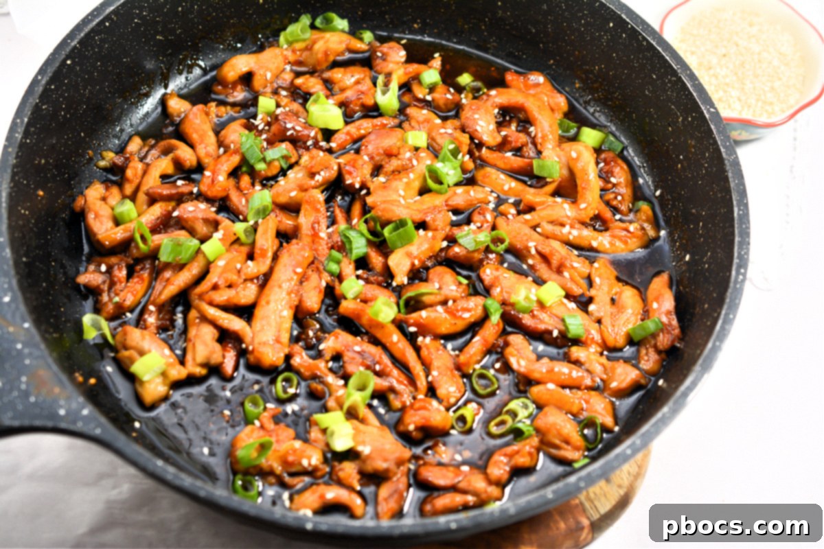 Sticky Keto Garlic Chicken served in a pristine white bowl, beautifully garnished with fresh green onions and sesame seeds.