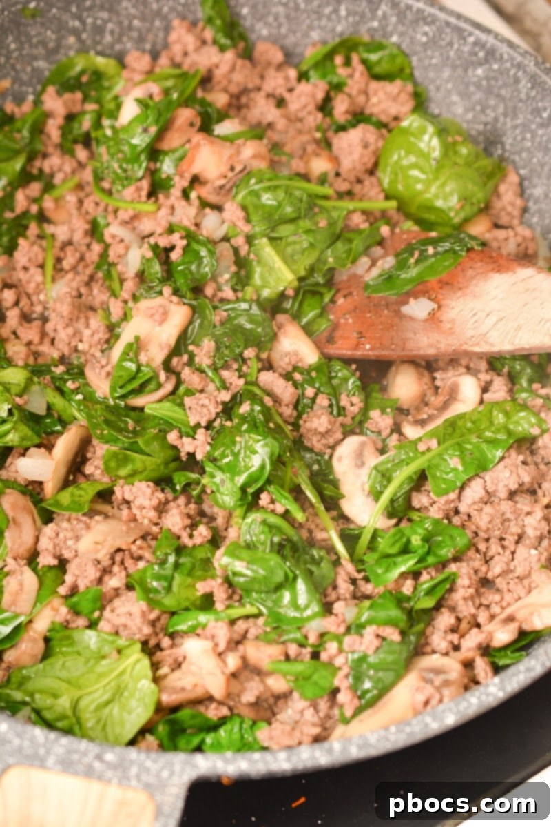 Ultimate Cheesy Keto Beef, Spinach & Mushroom Feast 5 Fresh spinach being mixed into a skillet of ground beef and mushrooms, a key step in this keto casserole.
