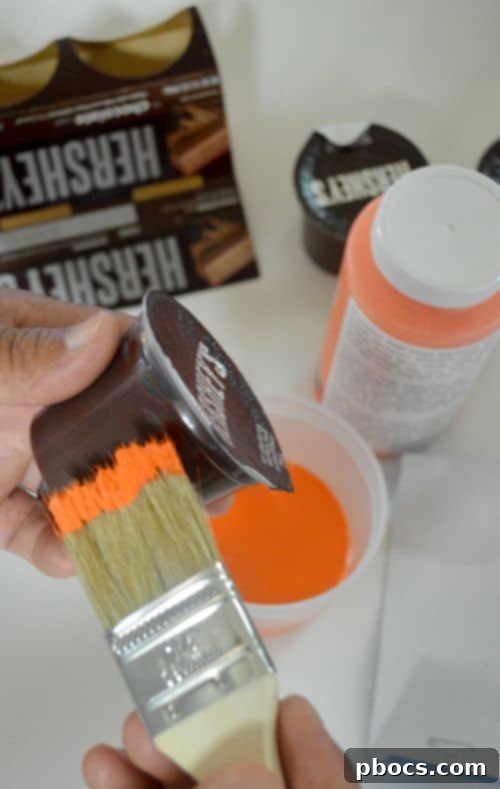 Applying first coat of orange paint to a Hershey's pudding cup for pumpkin craft