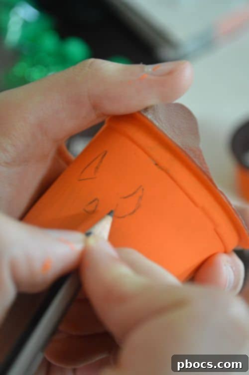 Drawing pumpkin faces with a pencil on painted pudding cups, close-up of hands
