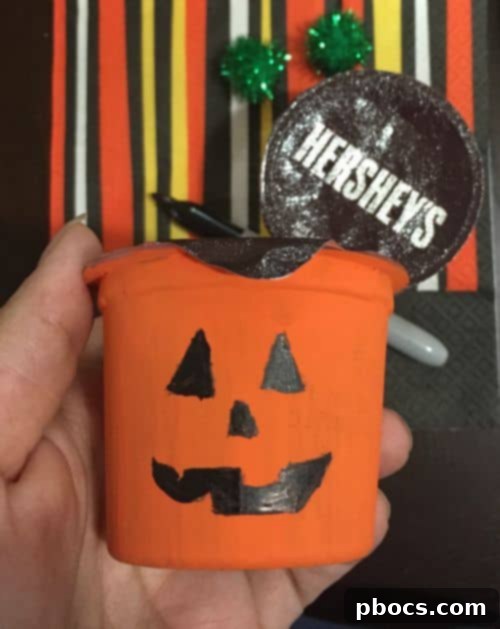 Coloring in pumpkin faces with a permanent marker on painted pudding cups