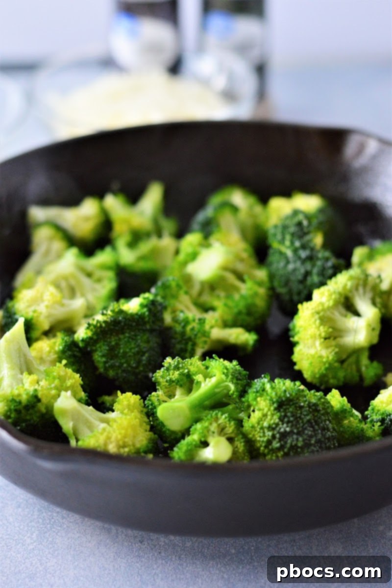 Creamy Low-Carb Chicken Alfredo 10 Broccoli cooking in a skillet with a splash of water.
