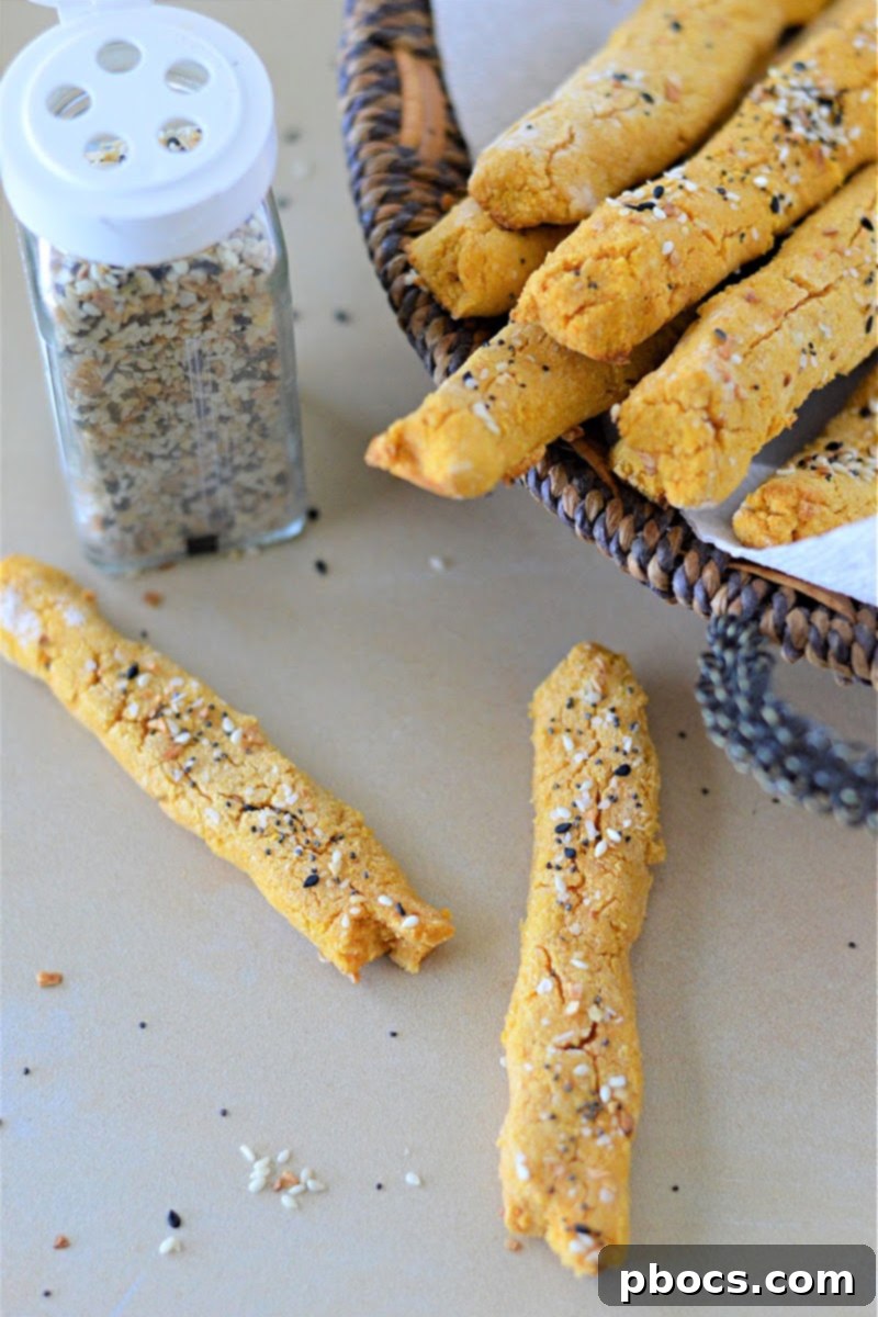 Hands sprinkling Everything Bagel Seasoning on Low Carb Pumpkin Breadsticks