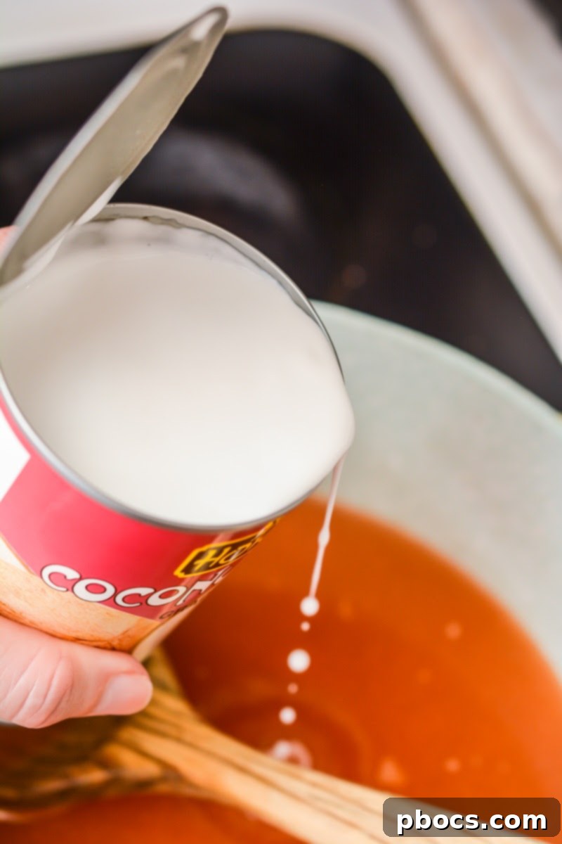 Pouring chicken broth and coconut milk into the pot to form the soup base