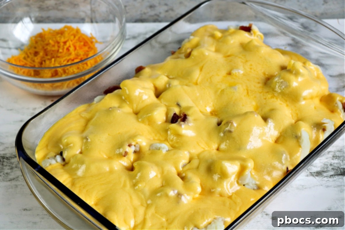 Keto Cauliflower Au Gratin in a casserole dish, topped with cheese and bacon, ready for baking.