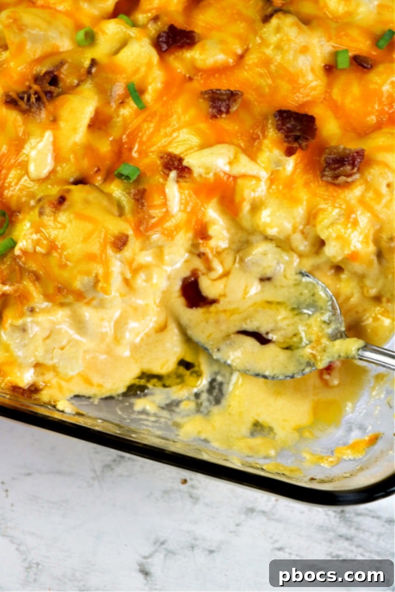 A serving spoon lifting a scoop of creamy Keto Cauliflower Au Gratin from a casserole dish.