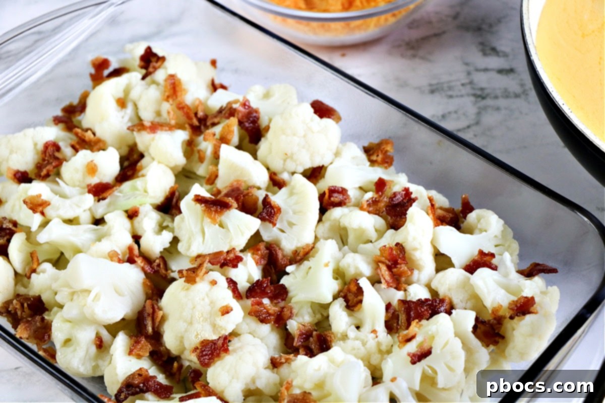The second layer of Keto Cauliflower Au Gratin in the casserole dish, showing bacon sprinkled over cauliflower.