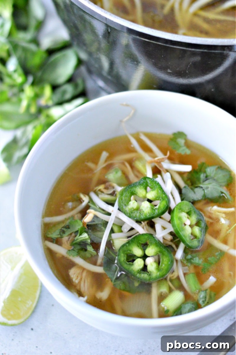 A steaming bowl of low-carb chicken pho with fresh herbs and lime wedges, ready to eat.