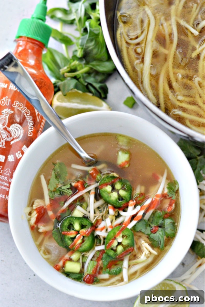 A bowl of low-carb chicken pho with various fresh toppings like cilantro, lime, and chili sauce.